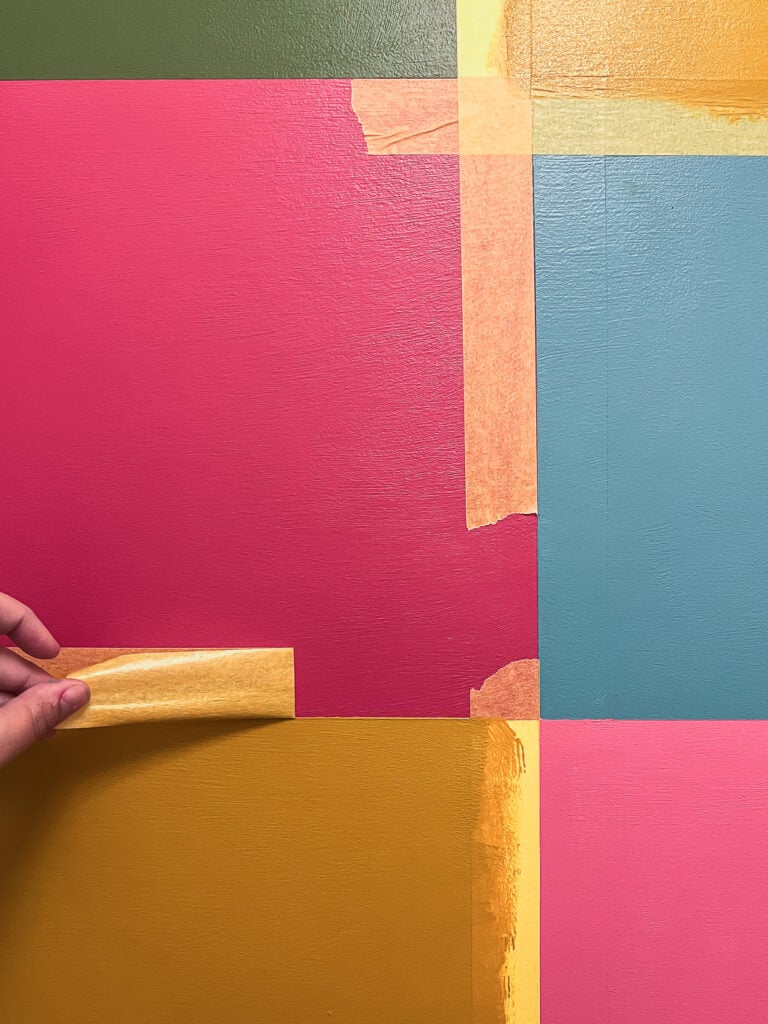 Photo of color block wall mural in colorful hues with woman's hand peeling off yellow painter's tape